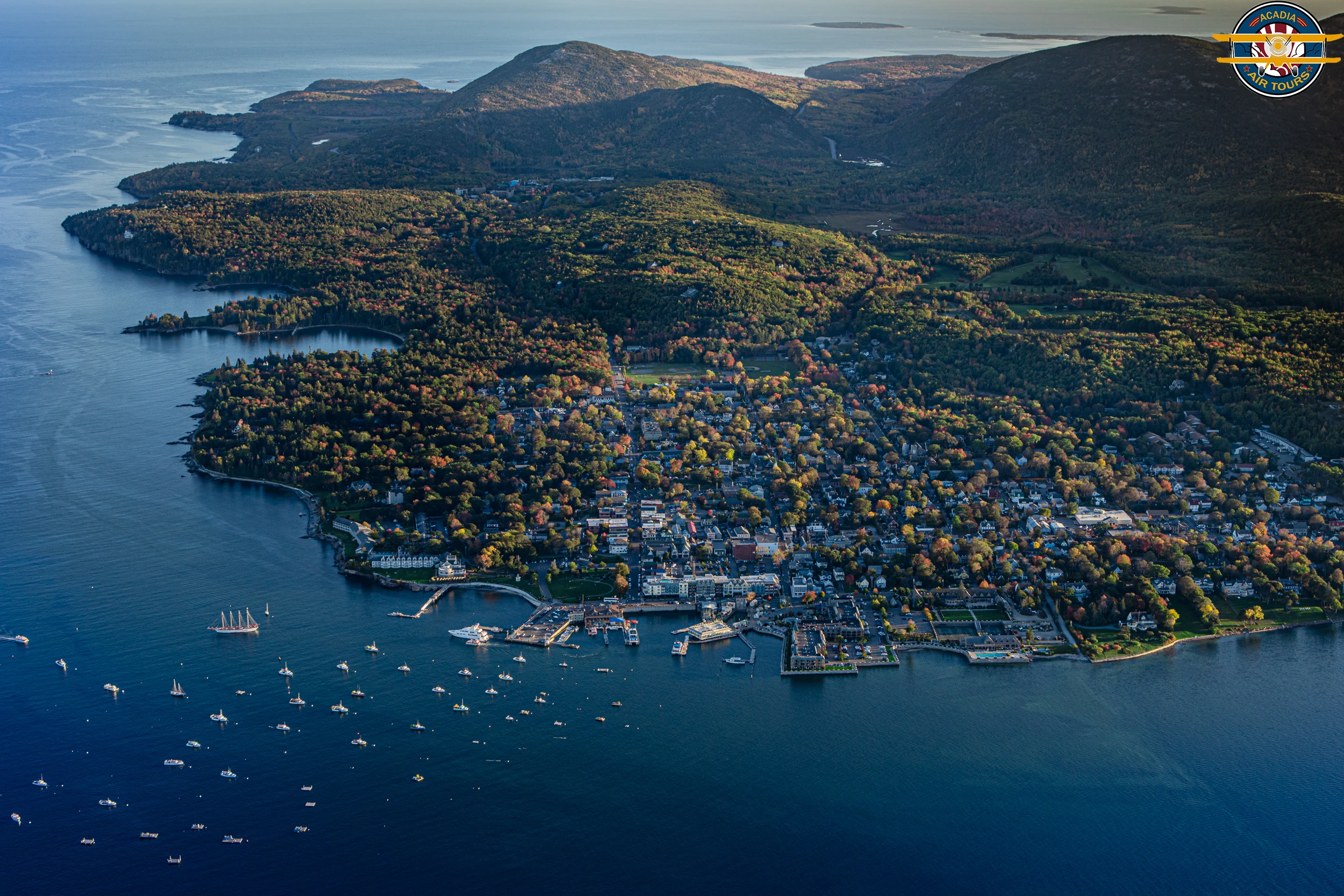 Aerial view of Bar Harbor, Maine, with Frenchman Bay in the foreground and the hills of Acadia National Park in the background.