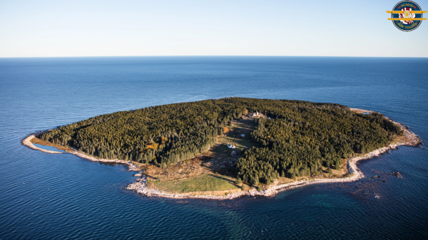 Remote Island off the Coast of Maine – Aerial Perspective Aerial view of a forested island surrounded by deep blue ocean, with clear shoreline and scattered small buildings.