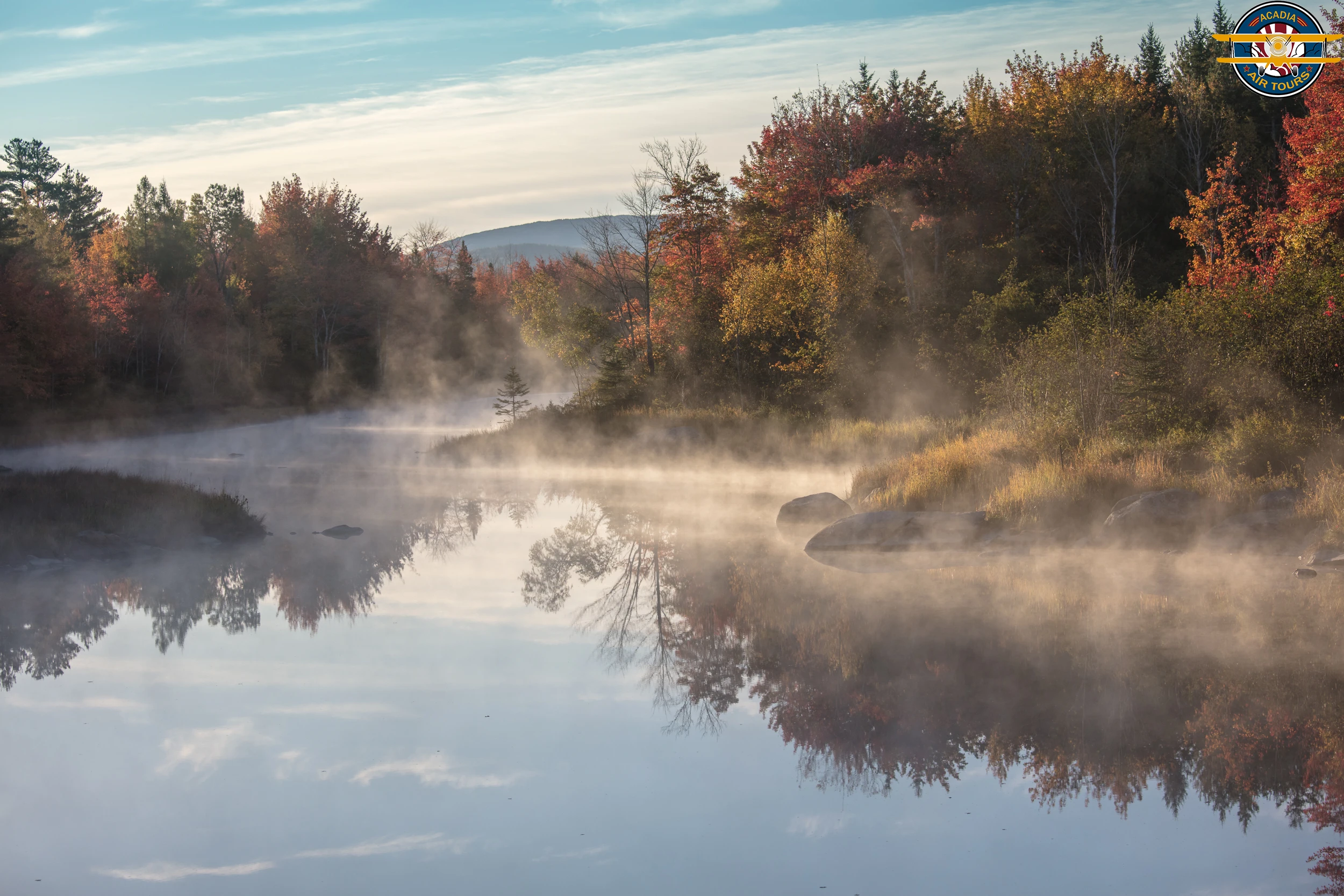 Morning mist over a calm river surrounded by autumn trees in Acadia National Park.