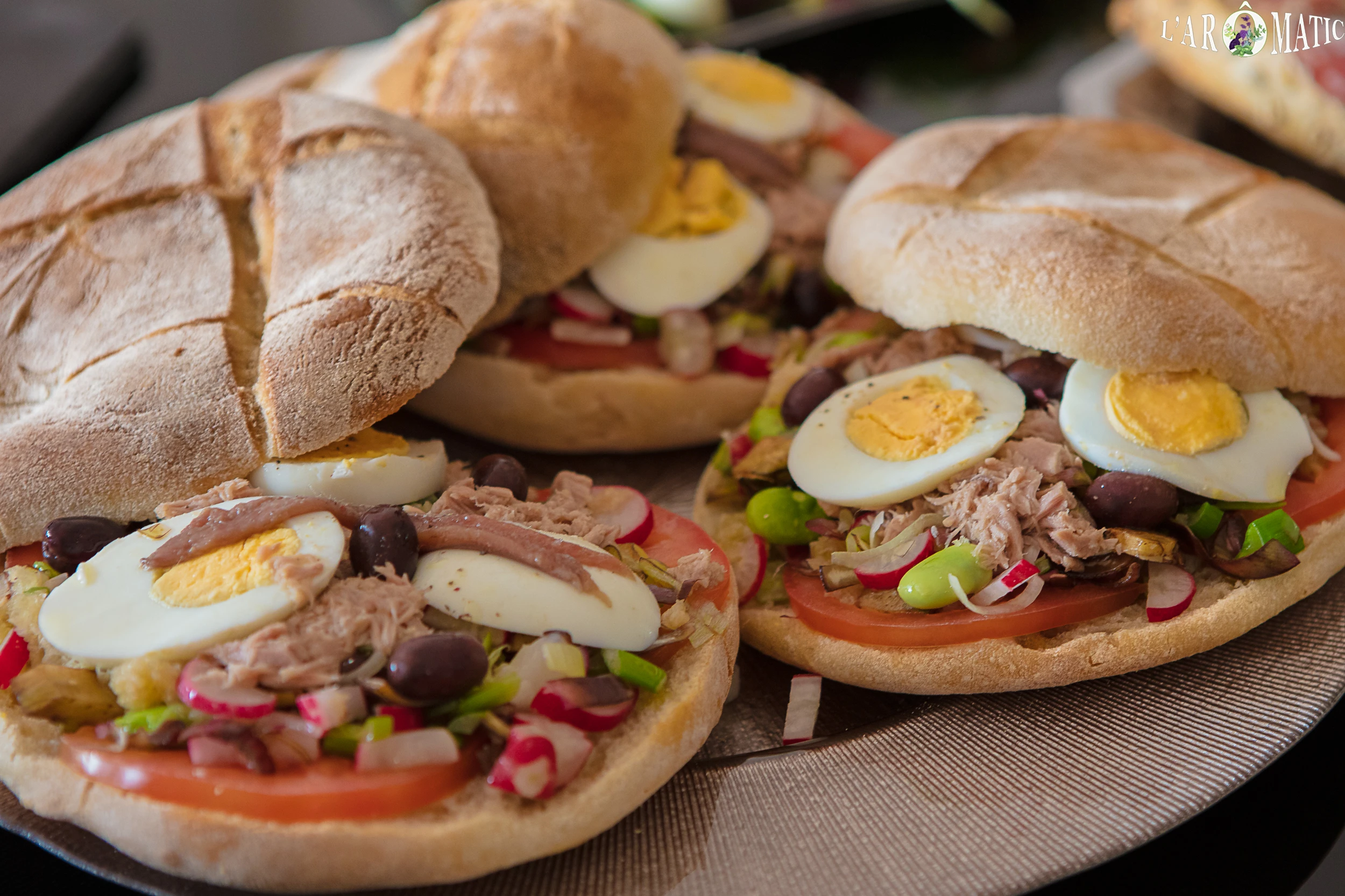 Close-up of freshly prepared Pan Bagnat sandwiches with tuna, eggs, olives, and vegetables.