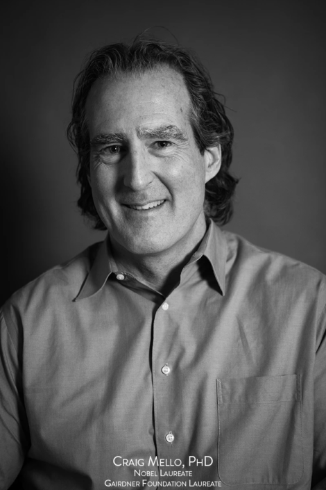 Portrait of Craig Mello, PhD, smiling in a studio-lit black and white photograph.