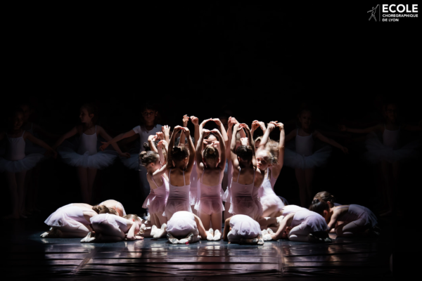 Year-end ballet recital – Group choreography on stage Young ballet students performing in soft lighting on stage during a year-end recital at École Chorégraphique de Lyon.