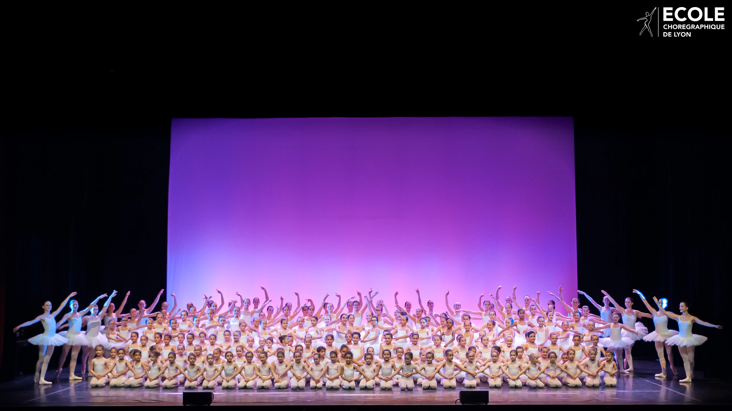 Group photo of ballet students on stage during a recital at École Chorégraphique de Lyon, with a purple-lit backdrop.