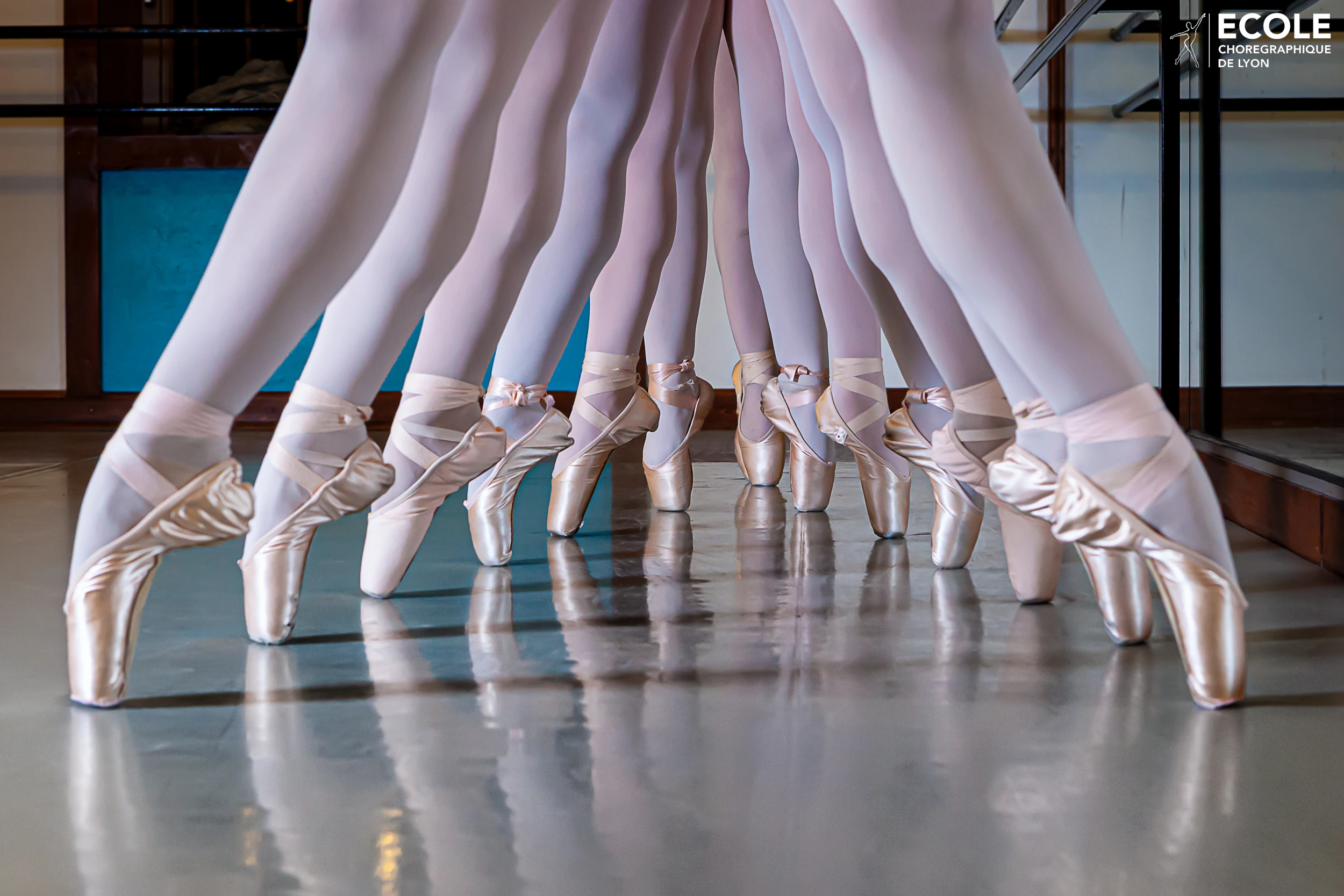 Close-up of ballet dancers en pointe in a studio at École Chorégraphique de Lyon, with perfect alignment and mirrored reflection.