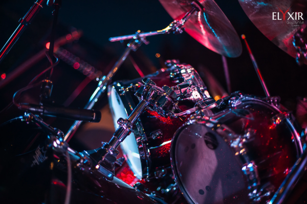 Drum kit in concert lighting – Elyxir live performance Close-up of a red sparkle drum set illuminated by colorful stage lights during a live concert.