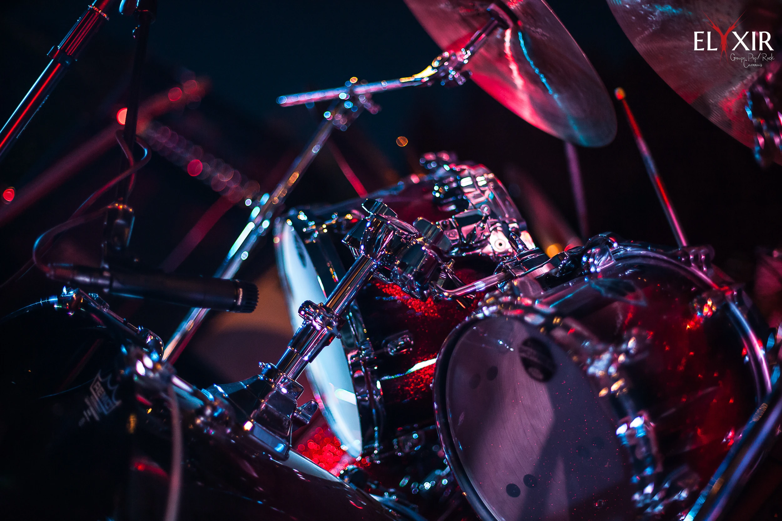 Close-up of a red sparkle drum set illuminated by colorful stage lights during a live concert.