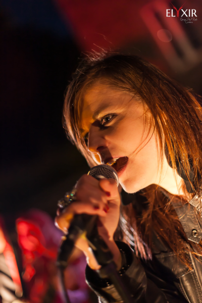 Live performance – Aurélie singing under spotlight Close-up of singer Aurélie passionately performing live on stage, holding a microphone under dramatic lighting.
