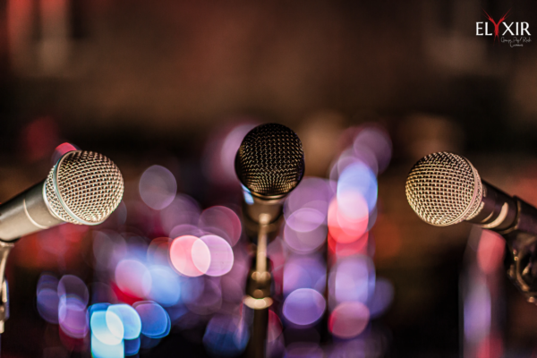 Microphones on stage – concert setup with ambient lighting Three dynamic microphones in a row with colorful stage lights blurred in the background.