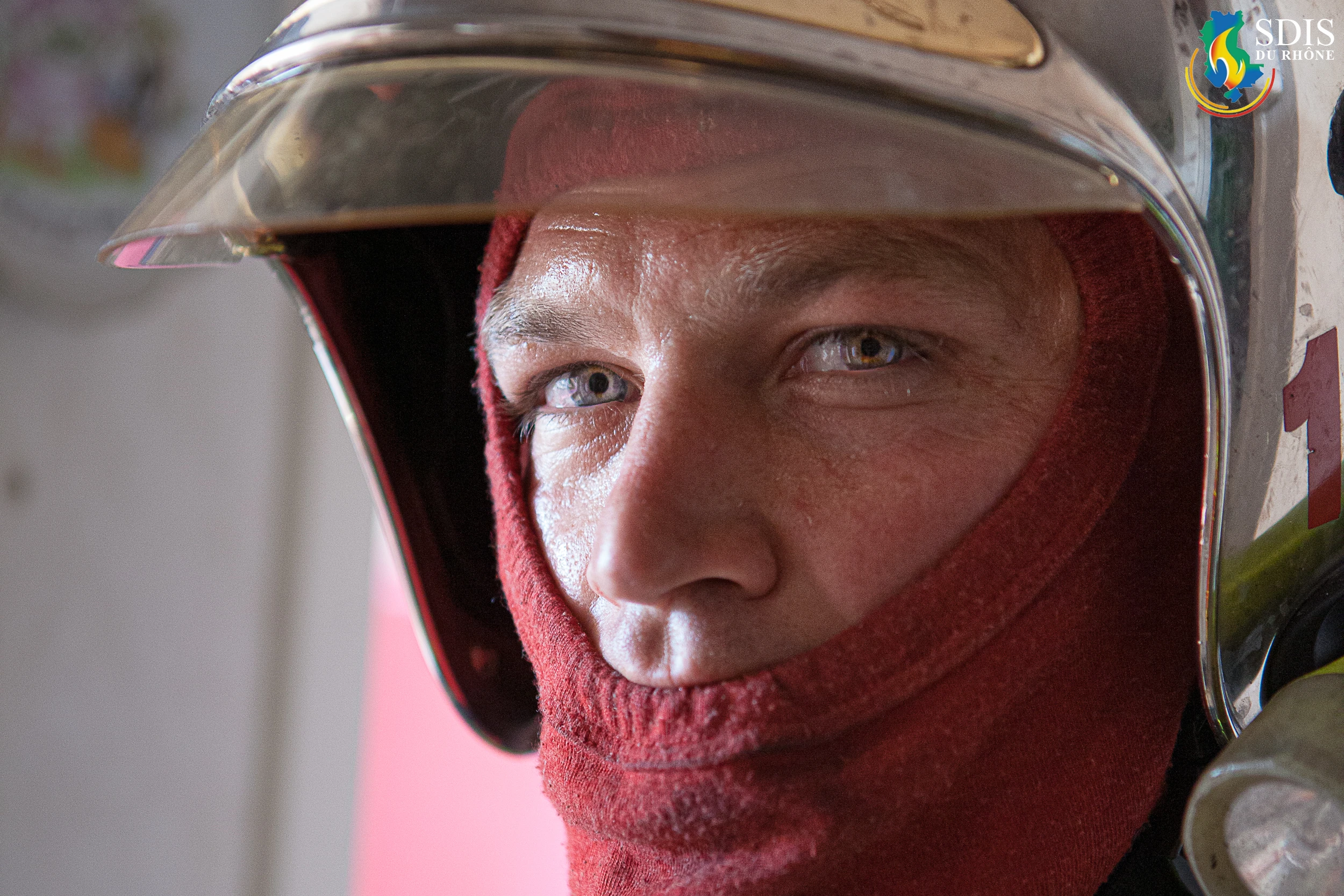 Close-up portrait of a firefighter from SDIS du Rhône wearing fire protection gear during a residential house fire response.