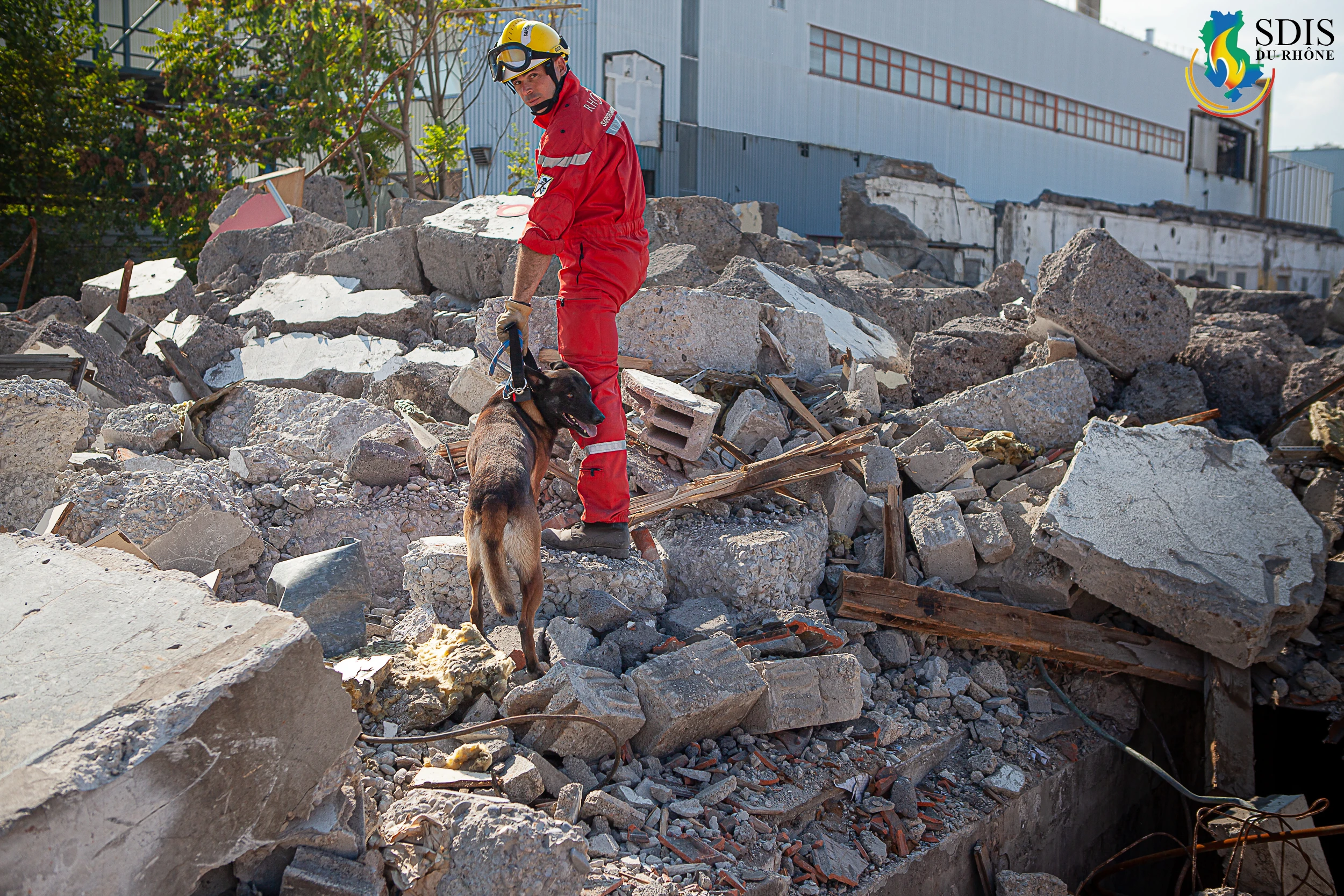 Firefighter from SDIS du Rhône with search and rescue dog navigating rubble after a structural collapse.