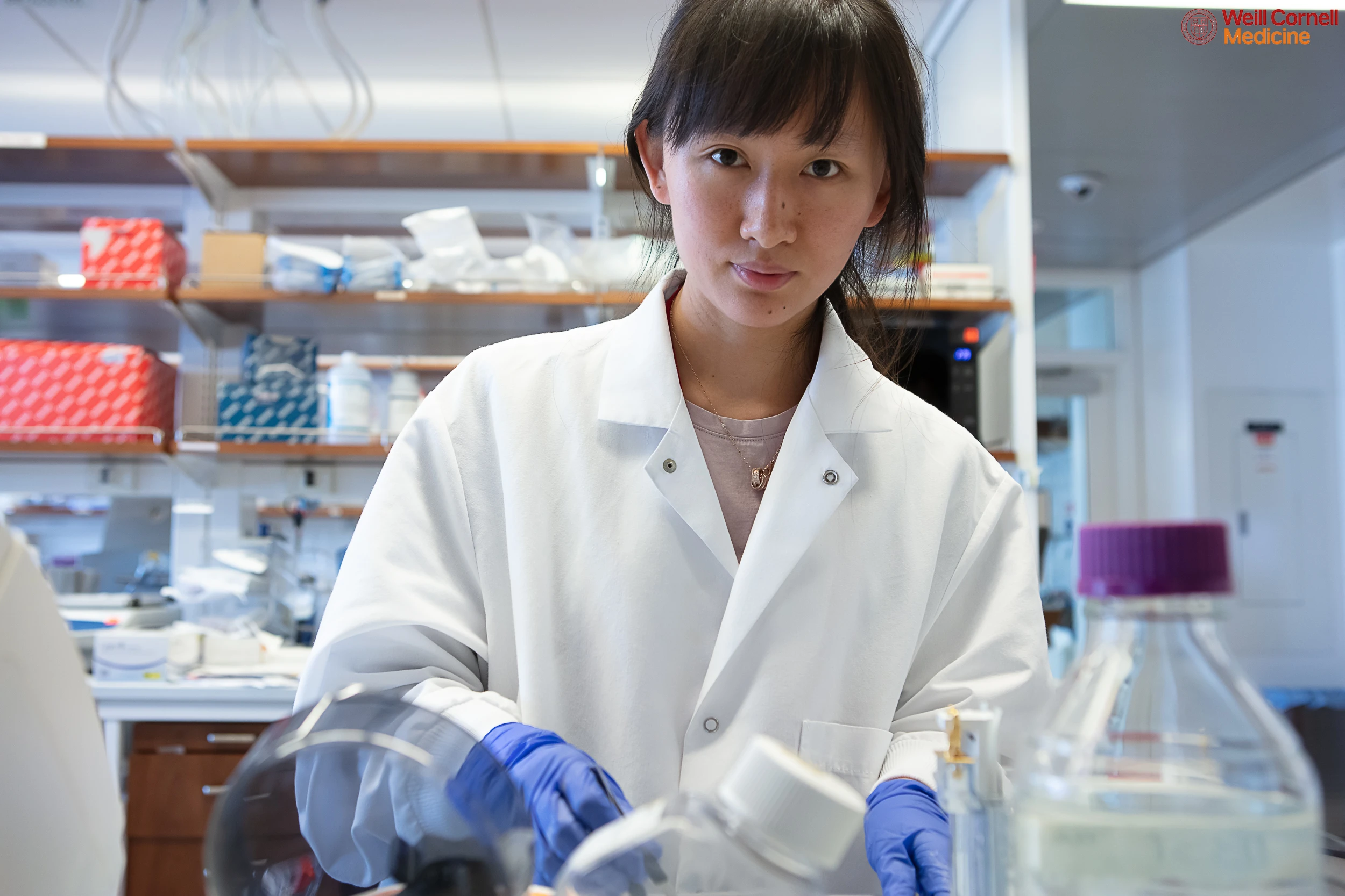 Young researcher in lab coat working at Weill Cornell Medicine.