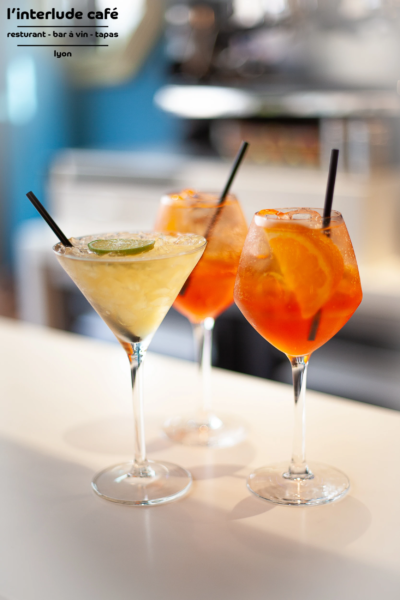 Signature Cocktails at L’interlude Café – Lyon Wine Bar Three colorful cocktails on a bar counter at L’interlude Café in Lyon.