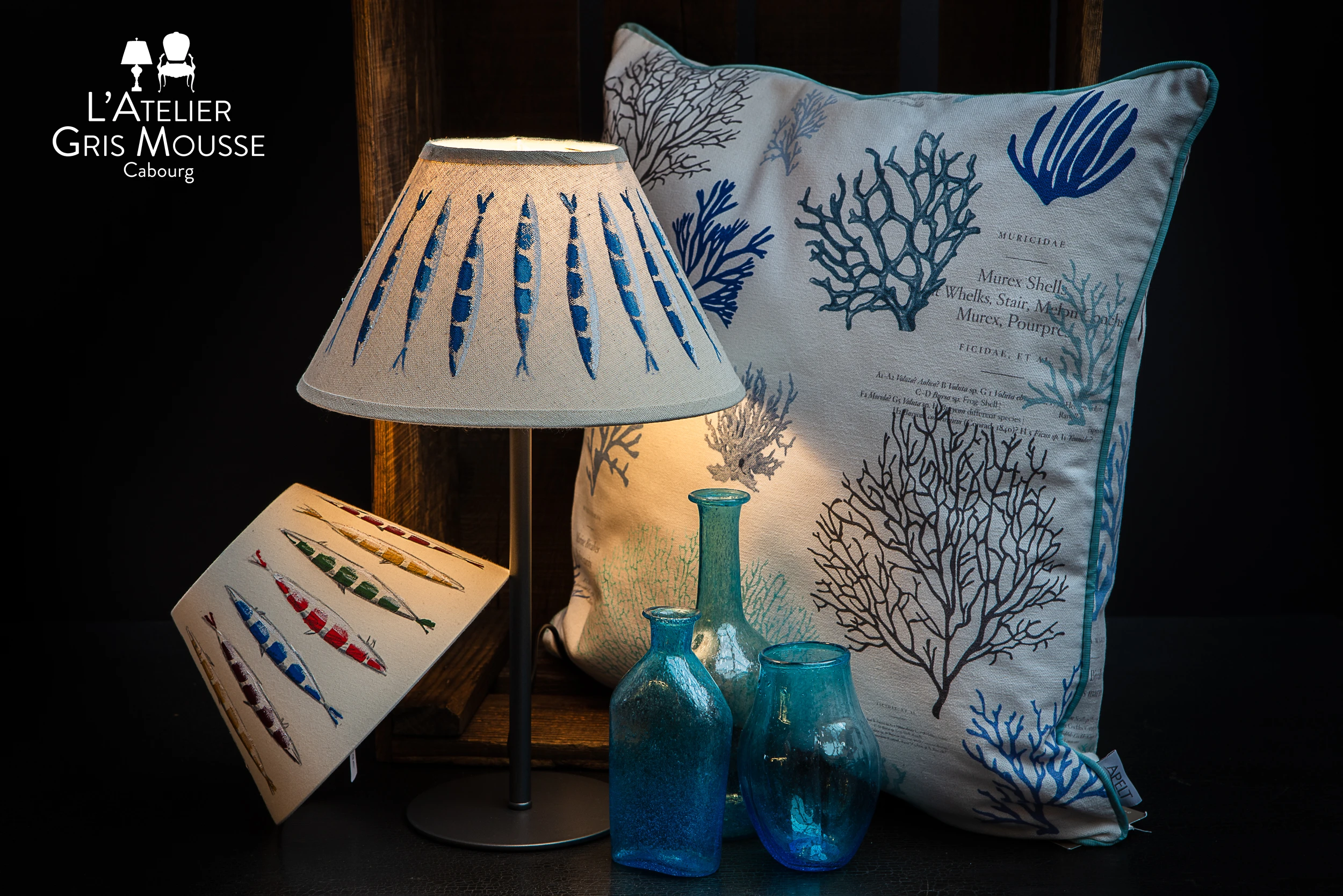 Seaside-themed cushion, fish-print lamp and blue glass vases – Atelier Gris Mousse studio composition
