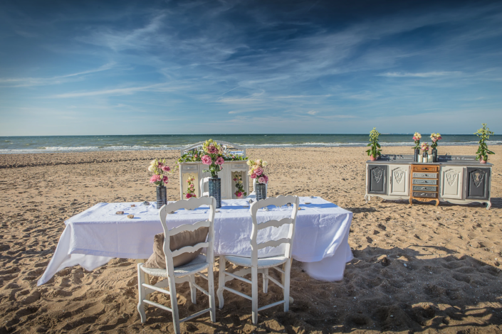 Outdoor dining scene on the beach with patinated furniture and floral arrangements – Atelier Gris Mousse campaign