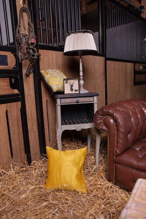 Rustic nightstand, yellow cushion, and vintage lighting in a styled horse stable — part of a creative visual identity for interior design by Atelier Gris Mousse.