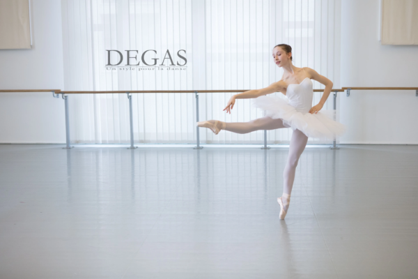 Ballet student in white tutu captured mid-pose in rehearsal Young ballet dancer performing a classical pose in a white tutu in a bright studio.