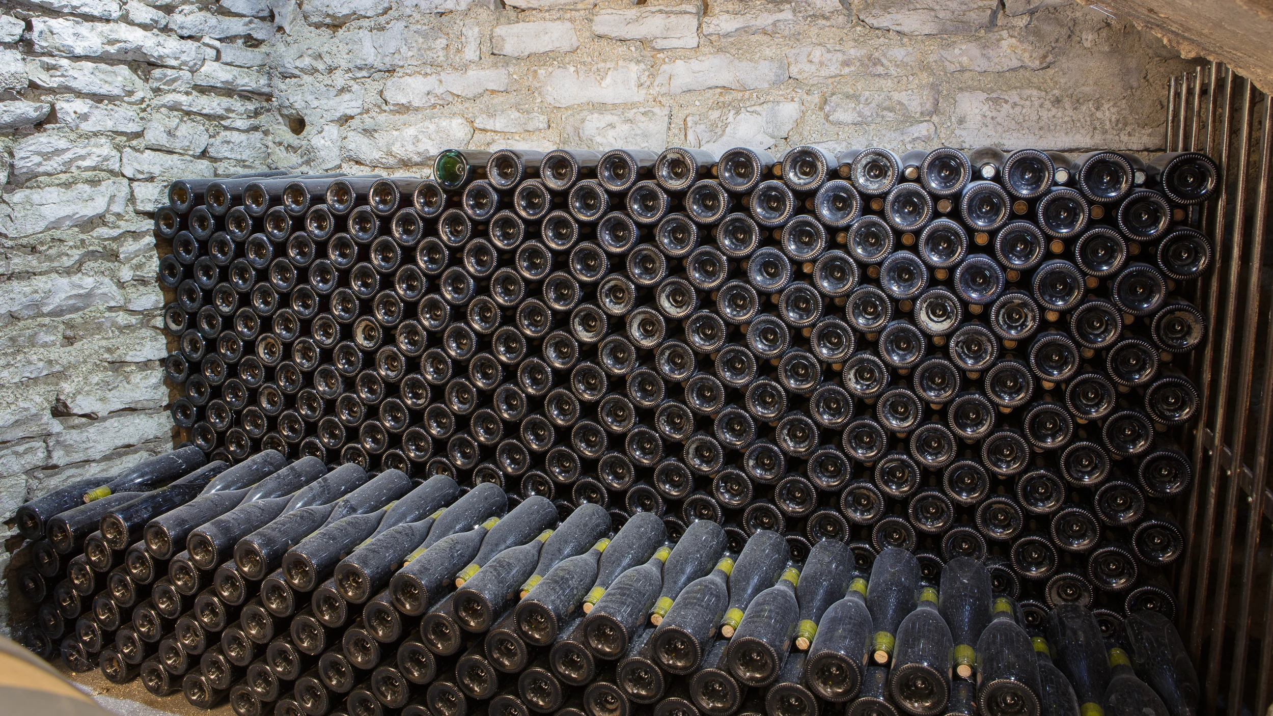 Dusty wine bottles stacked in a traditional stone cellar at Domaine Gros Frère et Sœur.