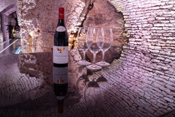 2014 Richebourg Grand Cru with Glasses – Domaine Gros Frère et Sœur Bottle of 2014 Richebourg Grand Cru wine with four empty glasses on reflective glass table in a historic Burgundy wine cellar.