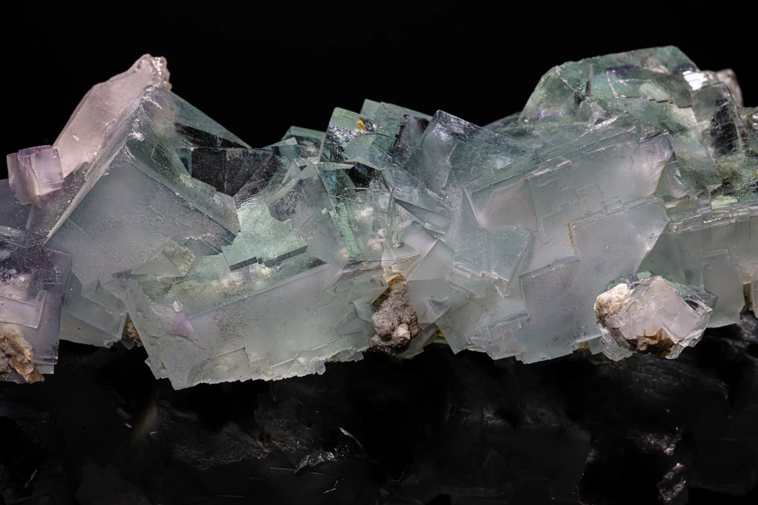 Close-up of translucent green and violet fluorite crystals with quartz on a reflective black base – De’An, Jiangxi, China.
