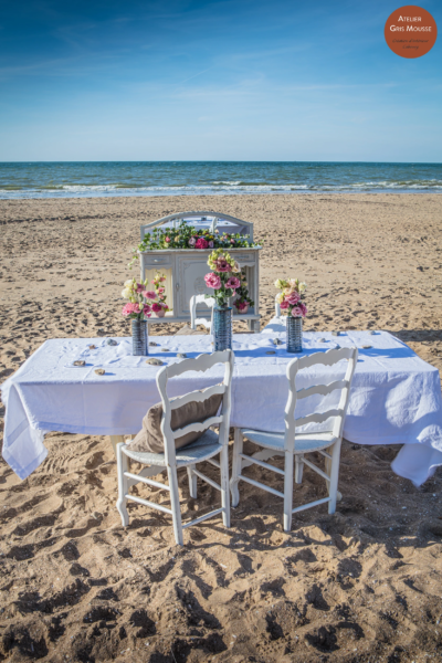 Beachside table set for two in front of a flower-topped sideboard, the sea in the background