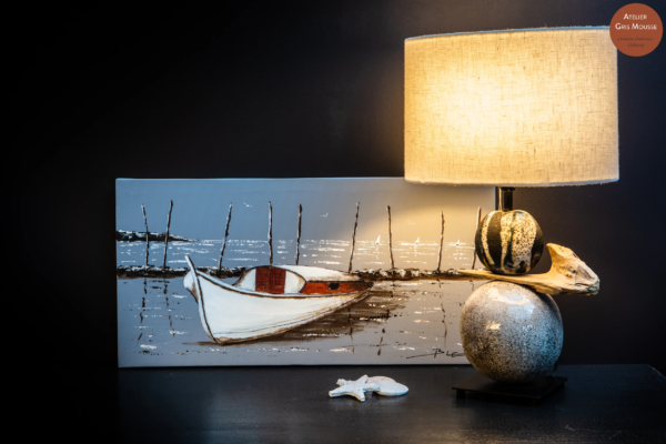 Painted canvas of a moored boat by Christian Bellec beside a raku ceramic and driftwood lamp with a linen shade