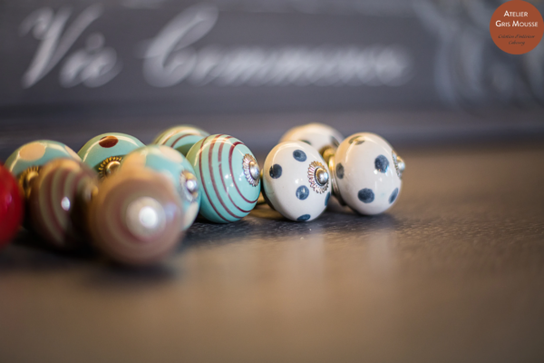 Row of hand-painted ceramic drawer knobs in stripes and polka dots, displayed on a dark lettered surface