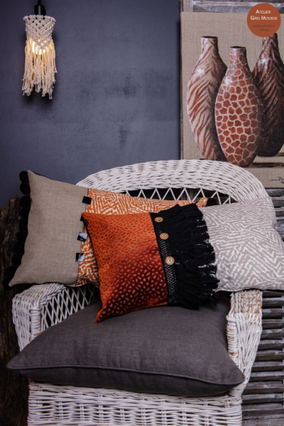 White rattan chair with earth-tone cushions in orange and animal prints, a macramé light and painted safari vases, an African-themed canvas by Christian Bellec behind