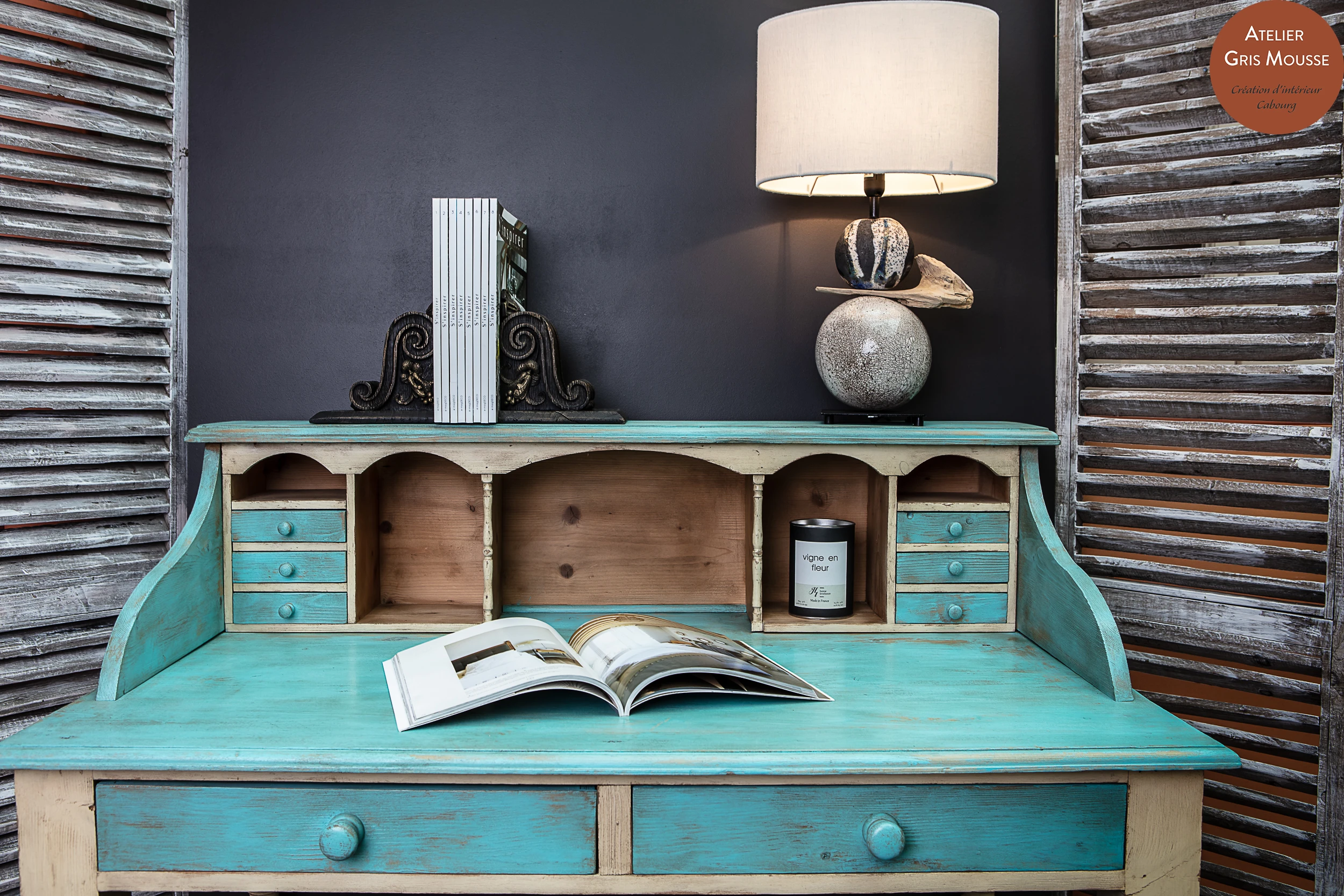 Distressed turquoise secretary desk with pigeonholes, a raku ceramic lamp, decorating magazines and patinated shutters on each side