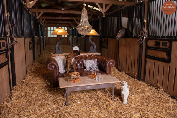 Boxer dog on a leather Chesterfield in a stable, a real horse looking out from its stall behind