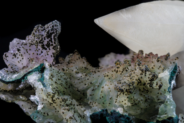 Macro view of a pale calcite crystal above a green and pink crust dotted with small dark spheres, Brazil