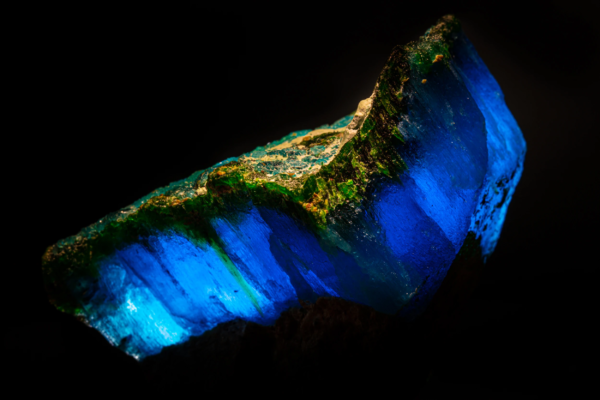Backlit krohnkite crystal glowing electric blue, edged with green natrochalcite crust, Chile