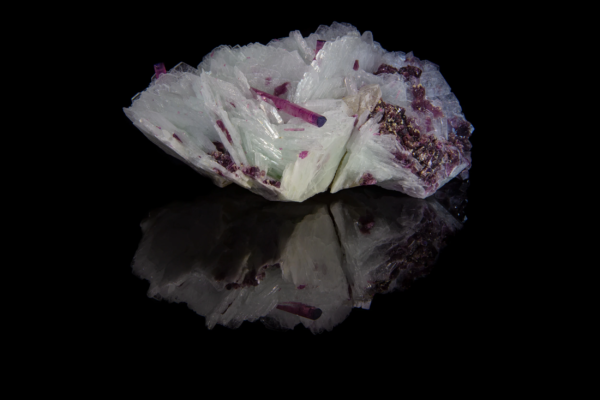 Deep pink tourmaline crystals lying across a fan of bladed white cleavelandite, mirrored on black vinyl, Brazil